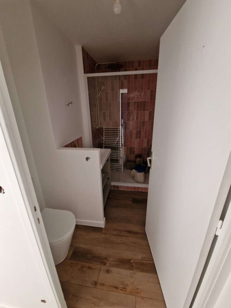 Salle de bain rénovée : douche carrelée en faïence terracotta, robinetterie dorée, sol façon parquet