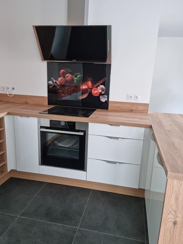 Cuisine posée : façades blanches laquées, plan de travail bois, four encastré, plaque à induction et hotte inclinée
